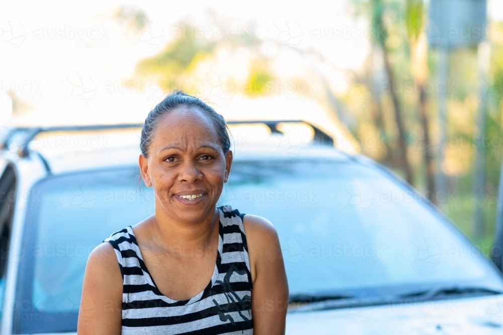 smiling middle-aged woman in from of vehicle with reflected light in Windscreen - Australian Stock Image