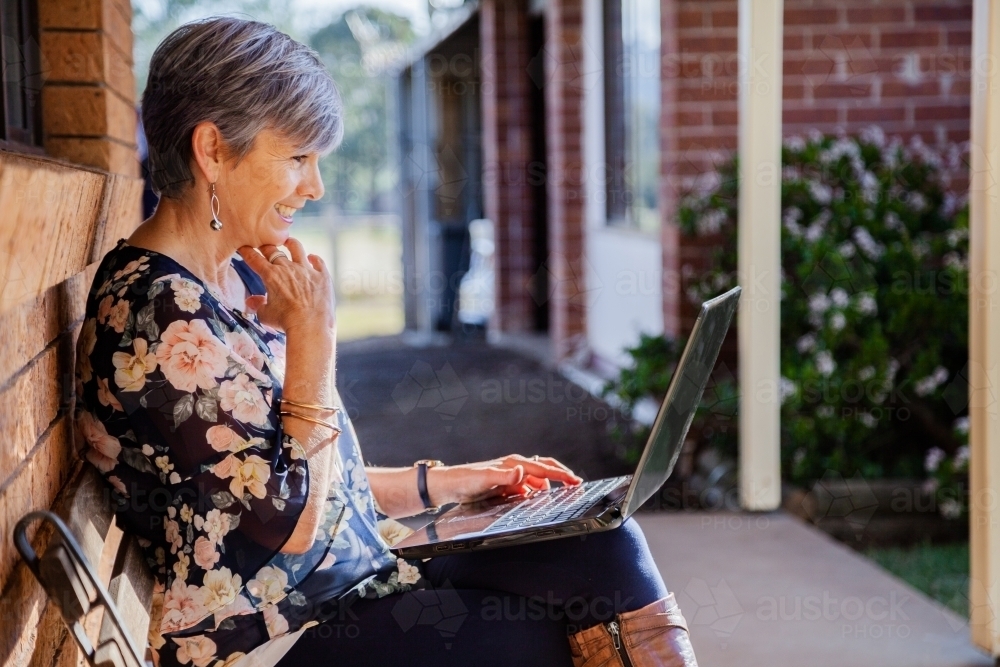 Smiling middle aged woman using her laptop to talk with grandkids - Australian Stock Image