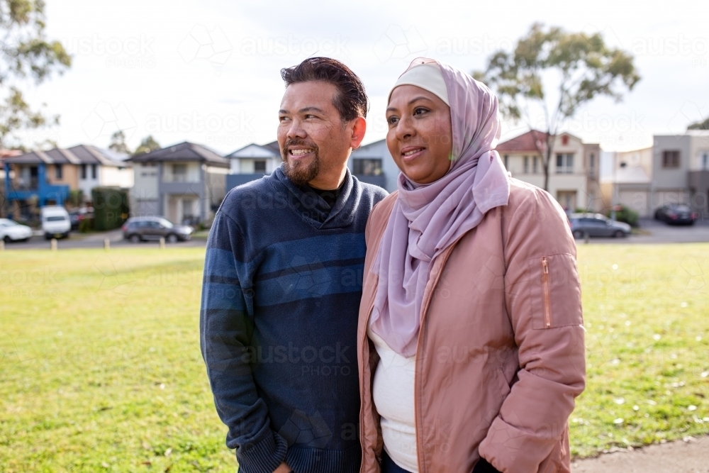 smiling middle aged woman wearing pink hijab and  middle aged man wearing blue sweater looking away - Australian Stock Image