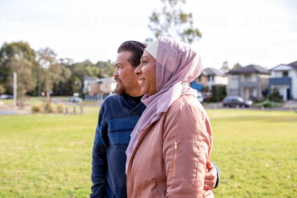 smiling middle aged woman wearing pink hijab and middle aged man wearing blue sweater looking away - Australian Stock Image