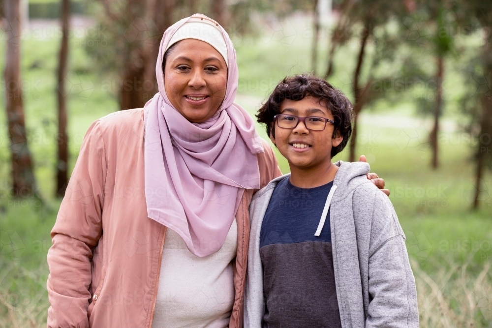 Smiling middle aged woman wearing pink hijab and smiling boy with curly hair wearing eye glasses - Australian Stock Image