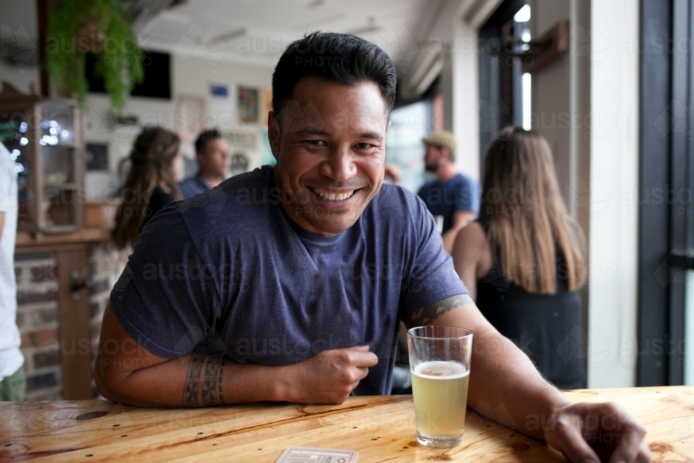 Smiling Polynesian man having a drink at a craft beer bar - Australian Stock Image