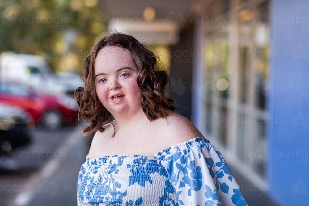 Smiling portrait of female teenager with down syndrome outside shops - Australian Stock Image