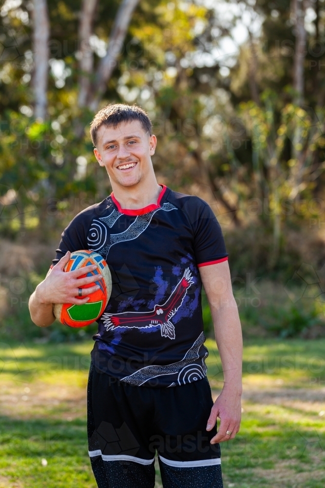 Smiling portrait of happy teenage Australian footy sports player holding football - Australian Stock Image