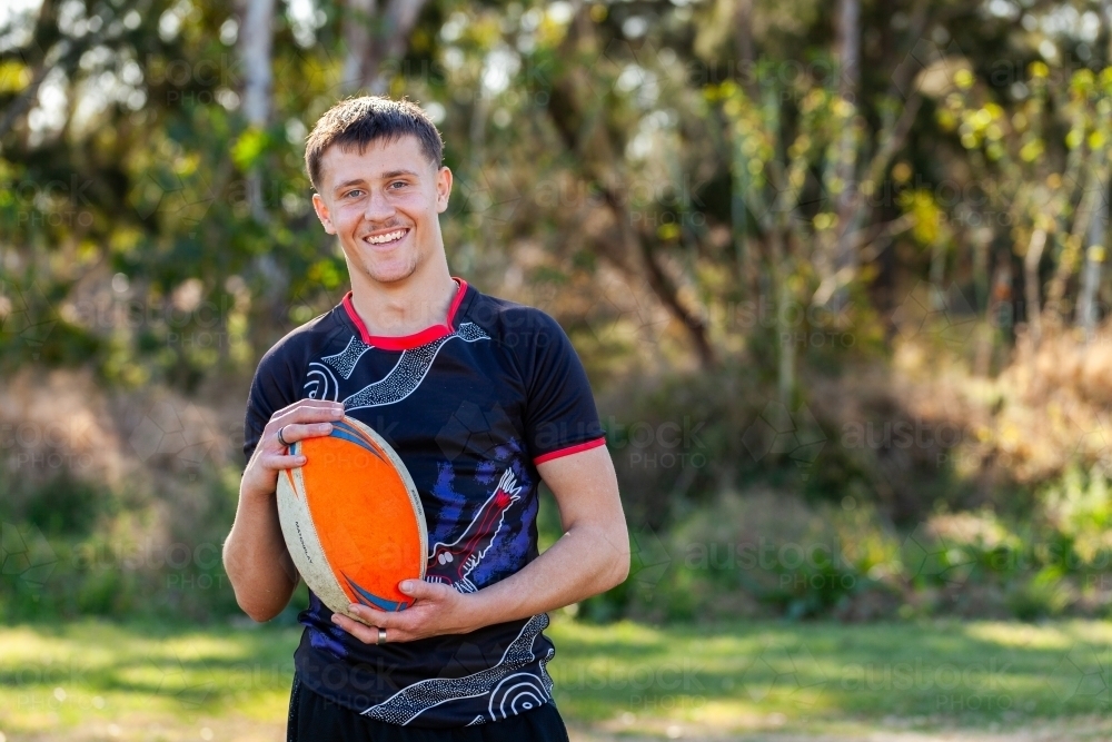Smiling portrait of happy teenage Australian footy sports player holding football - Australian Stock Image