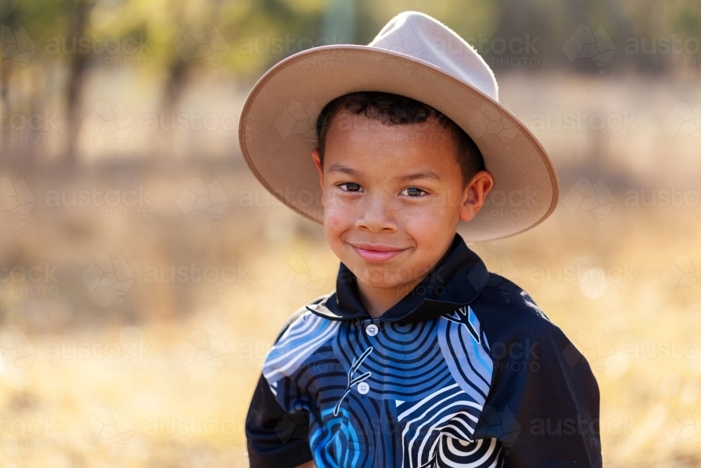 Smiling portrait of young aboriginal boy wearing hat outside in country setting - Australian Stock Image