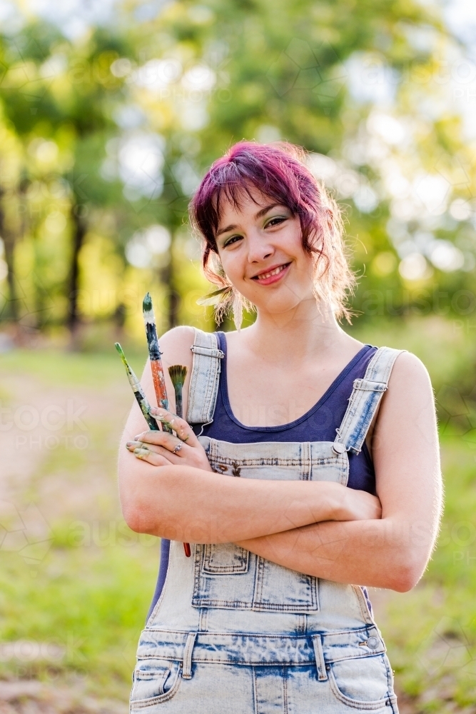 Smiling portrait of young woman artist painter holding art brushes - Australian Stock Image