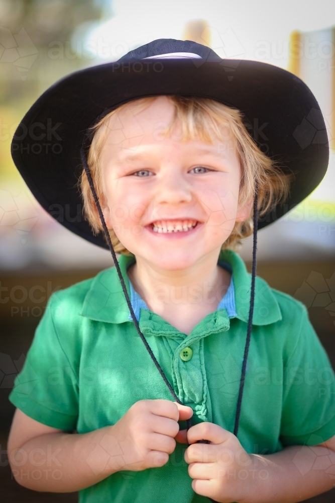 Smiling preschool boy wearing wide brim hat outdoors - Australian Stock Image