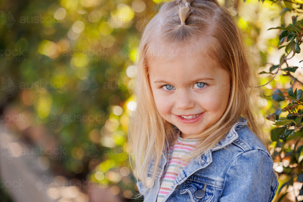 smiling preschool child sitting on edge of garden bed in bright sunny kindergarten yard - Australian Stock Image