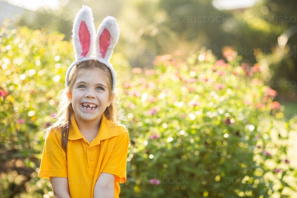 Smiling school kid outside in garden wearing rabbit ears for Easter celebrations - Australian Stock Image
