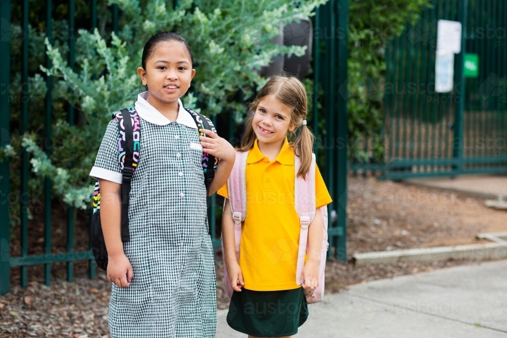 Smiling school kids outside public school with bags on - Australian Stock Image