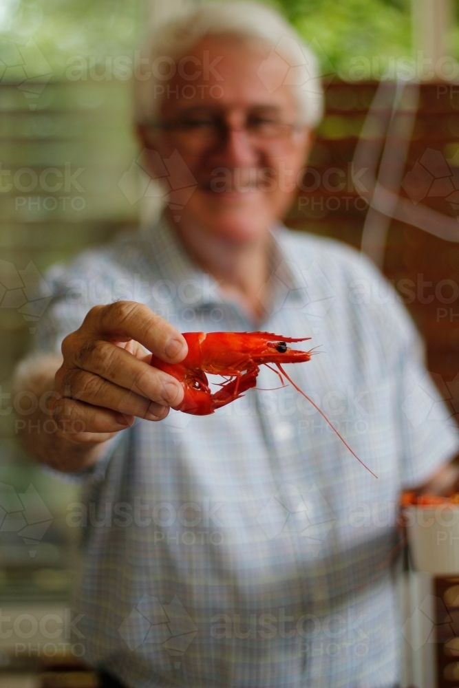 Smiling senior man holding out prawn - Australian Stock Image