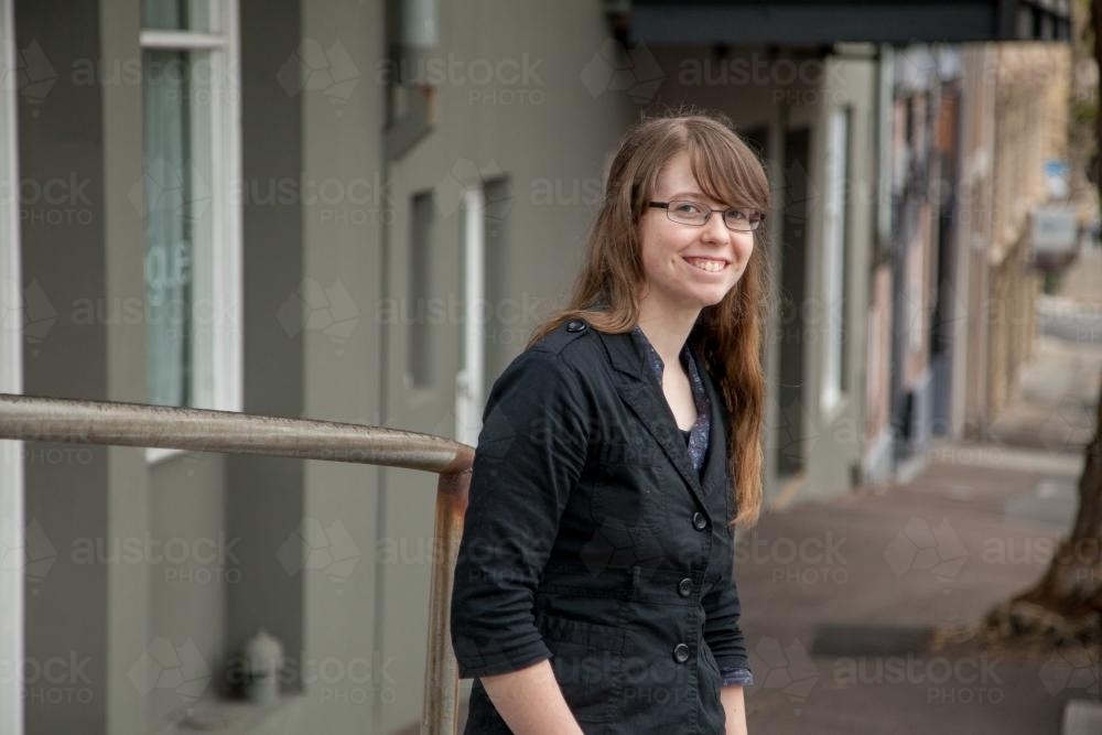 Smiling teen girl standing on overcast street beside road - Australian Stock Image
