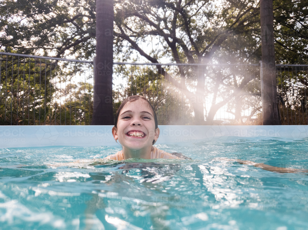 Smiling tween girl swimming in water of backyard pool grinning - Australian Stock Image