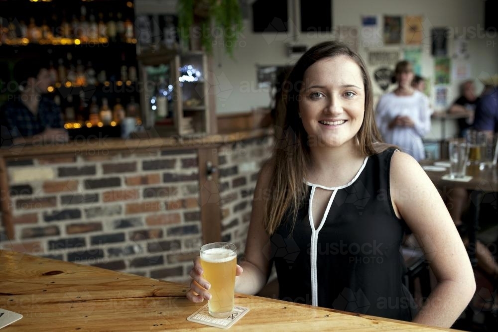 Smiling woman enjoying a drink at a local craft beer bar - Australian Stock Image