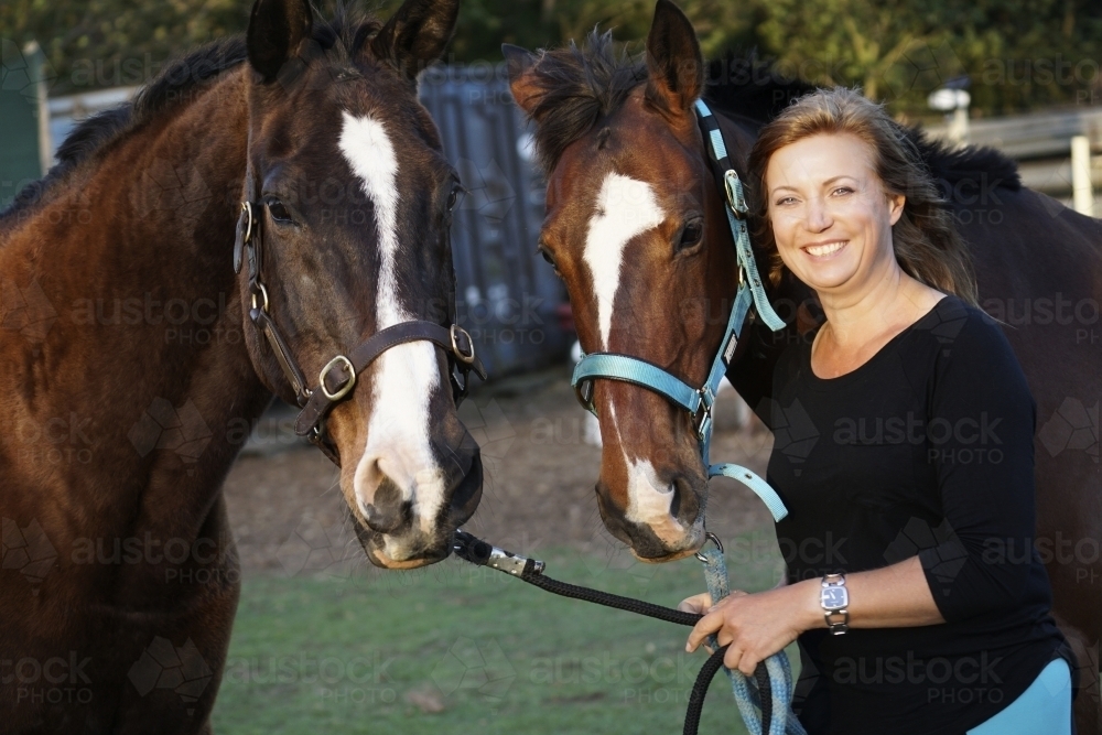 Smiling woman holding two horses - Australian Stock Image