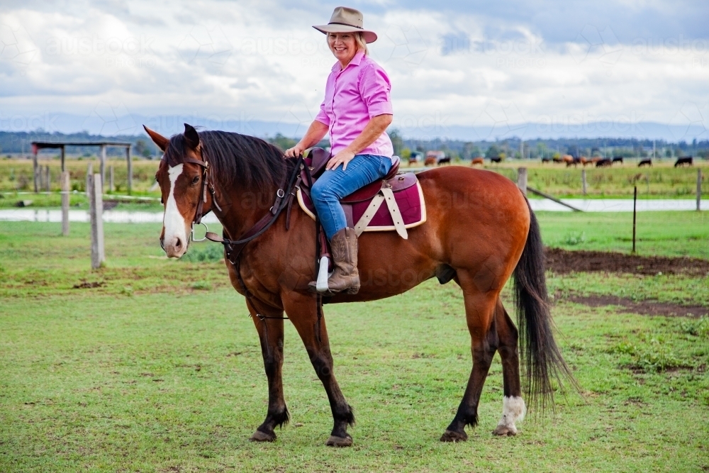 Smiling woman in hat riding her horse - Australian Stock Image