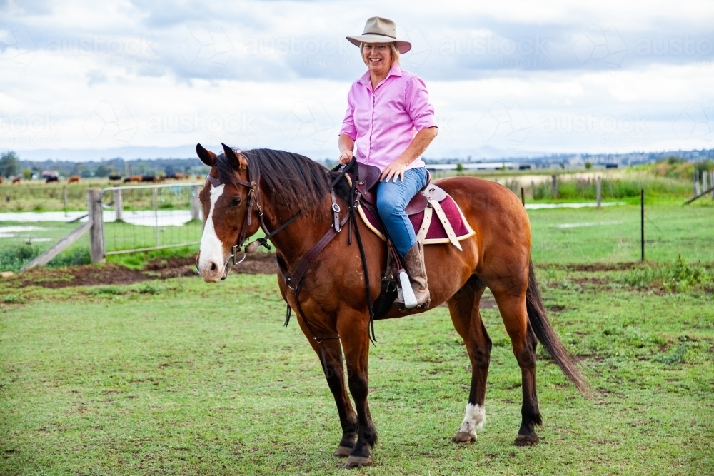 Smiling woman in hat riding her horse - Australian Stock Image