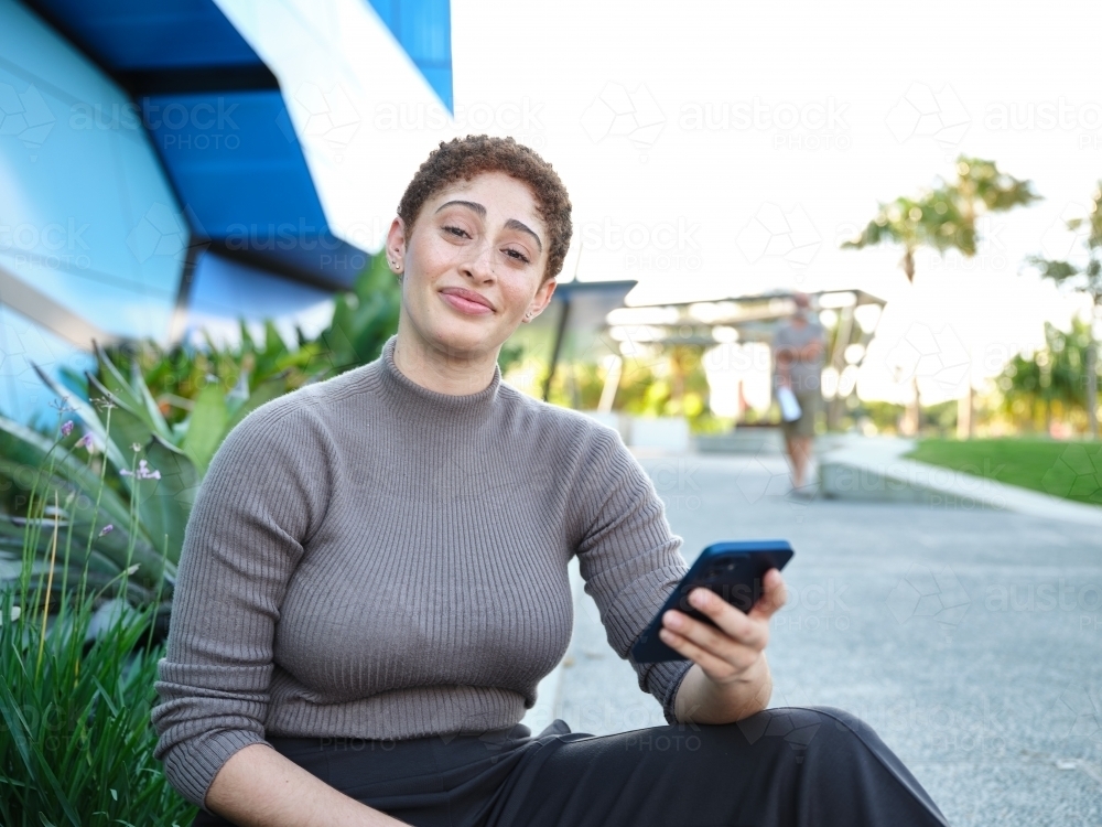 Smiling woman sitting outside using a phone - Australian Stock Image