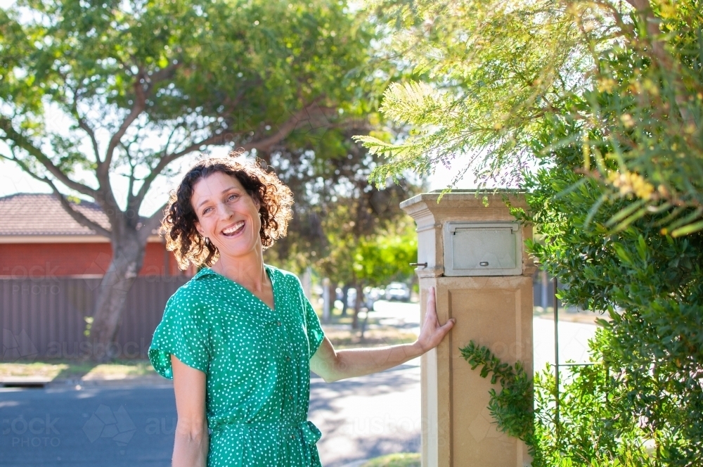 Smiling woman standing by mailbox at home - Australian Stock Image