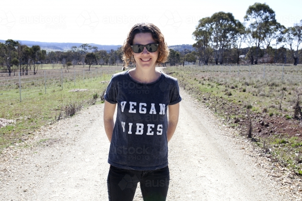 Smiling woman wearing vegan slogan t-shirt standing on rural dirt road - Australian Stock Image