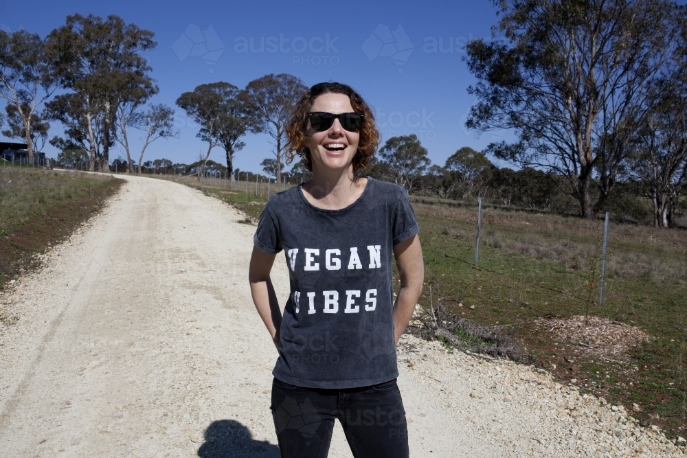 Smiling woman wearing vegan slogan t-shirt standing on rural dirt road - Australian Stock Image