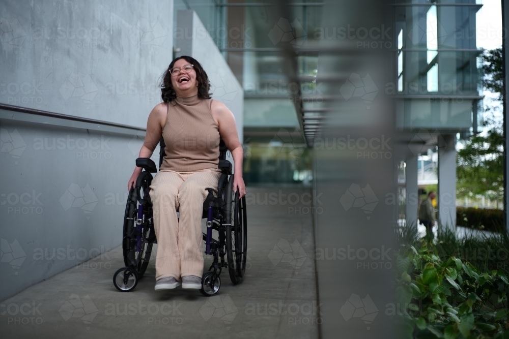 Smiling woman with a disability sitting in a wheelchair doing down the accessibility ramps - Australian Stock Image