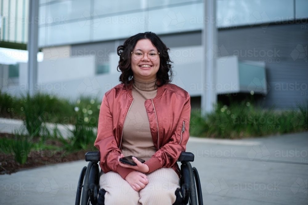 Smiling woman with a disability sitting in a wheelchair outside - Australian Stock Image