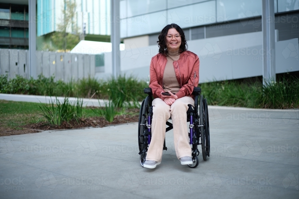Smiling woman with a disability sitting in a wheelchair outside - Australian Stock Image