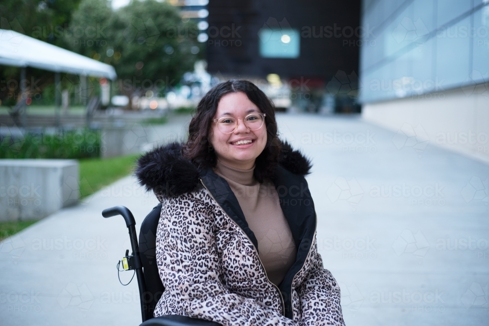 Smiling woman with a disability sitting in a wheelchair outside - Australian Stock Image