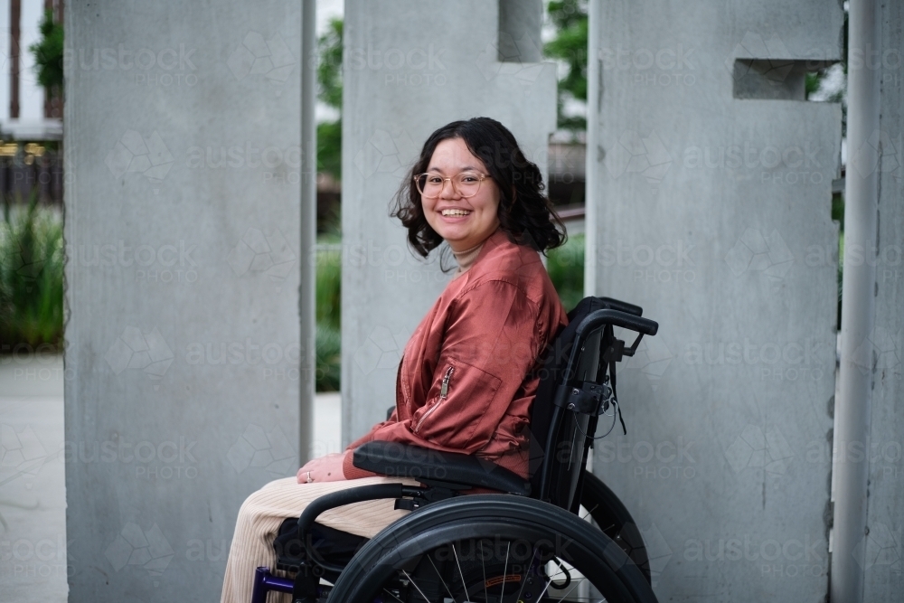 Smiling woman with a disability sitting in a wheelchair outside in urban setting - Australian Stock Image