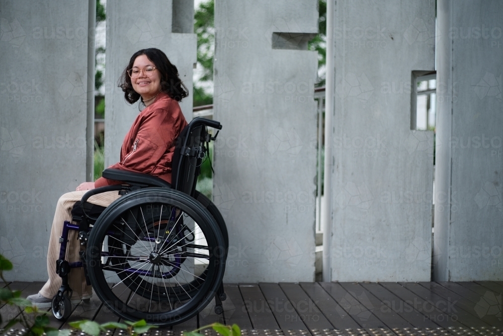 Smiling woman with a disability sitting in a wheelchair outside in urban setting - Australian Stock Image