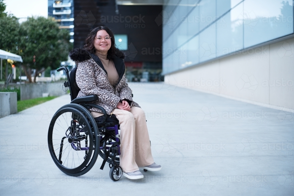 Smiling woman with a disability sitting in a wheelchair outside on cold day - Australian Stock Image