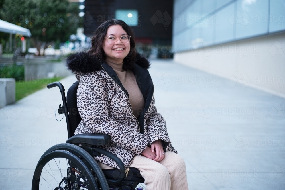 Smiling woman with a disability sitting in a wheelchair outside on cold day - Australian Stock Image