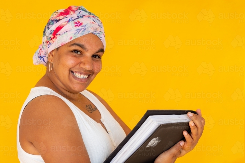 smiling woman with book on coloured yellow background - Australian Stock Image