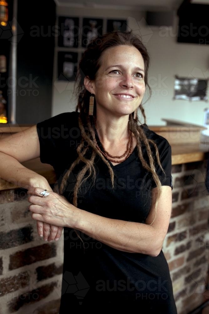 Smiling woman with dreadlocks resting against bar - Australian Stock Image