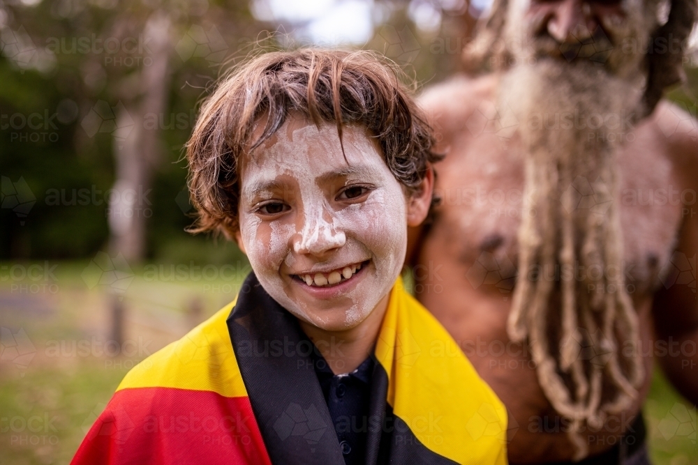 Smiling young Aboriginal boy wearing the Aboriginal flag and white face paint - Australian Stock Image