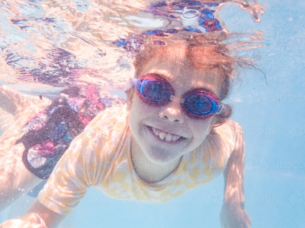 Smiling young Australian girl swimming in pool with goggles on in summer - Australian Stock Image