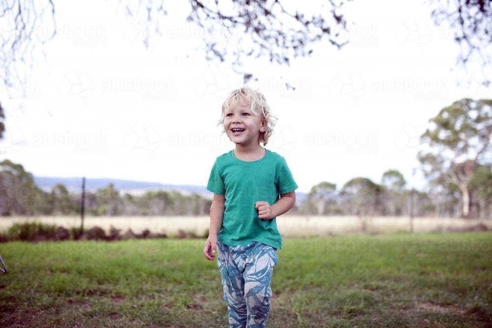 Smiling young boy outside wearing a green t-shirt - Australian Stock Image