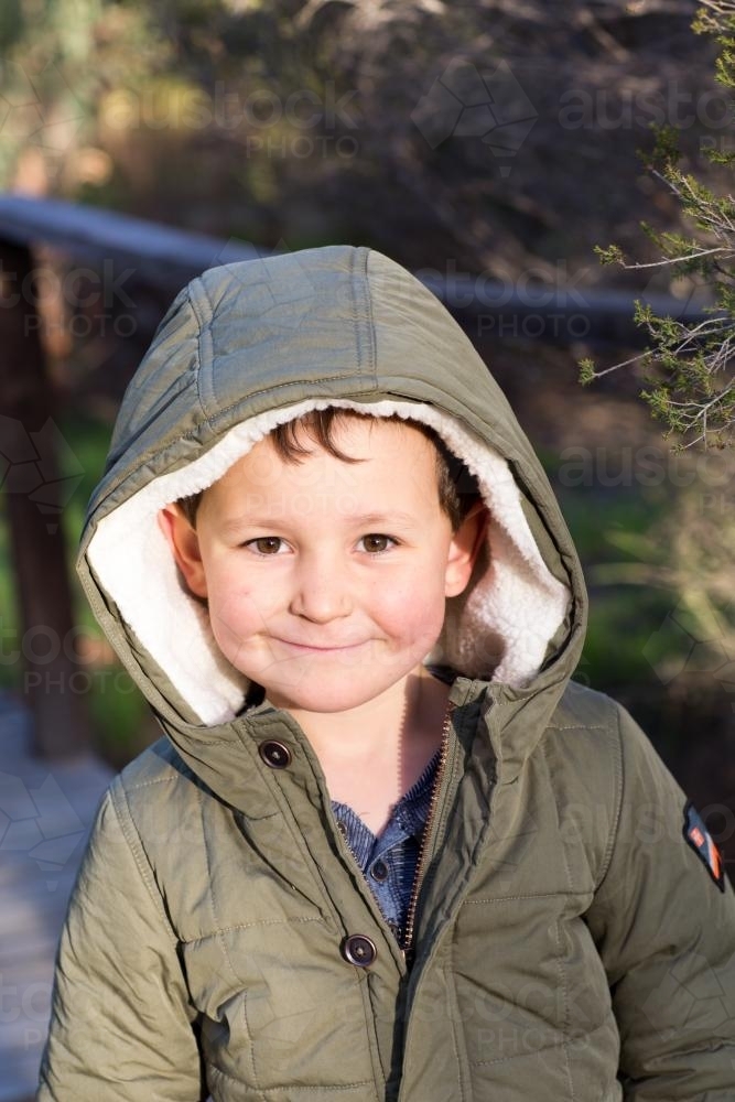 Smiling young boy wearing khaki hooded coat - Australian Stock Image