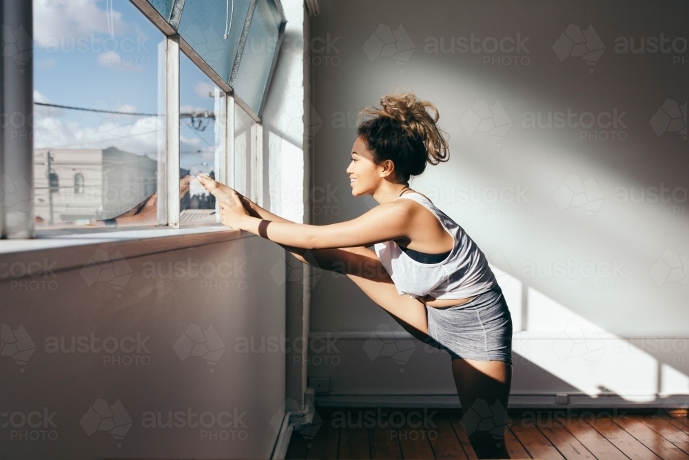 Smiling young female stretching her leg in a dance studio - Australian Stock Image
