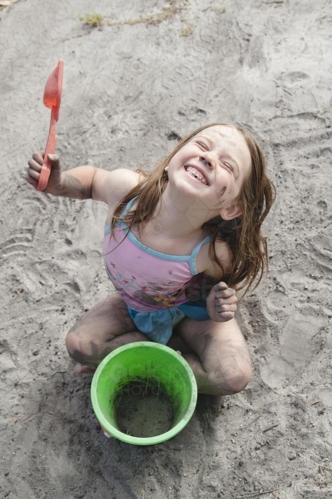Smiling young girl playing in dirt with a bucket and spade - Australian Stock Image