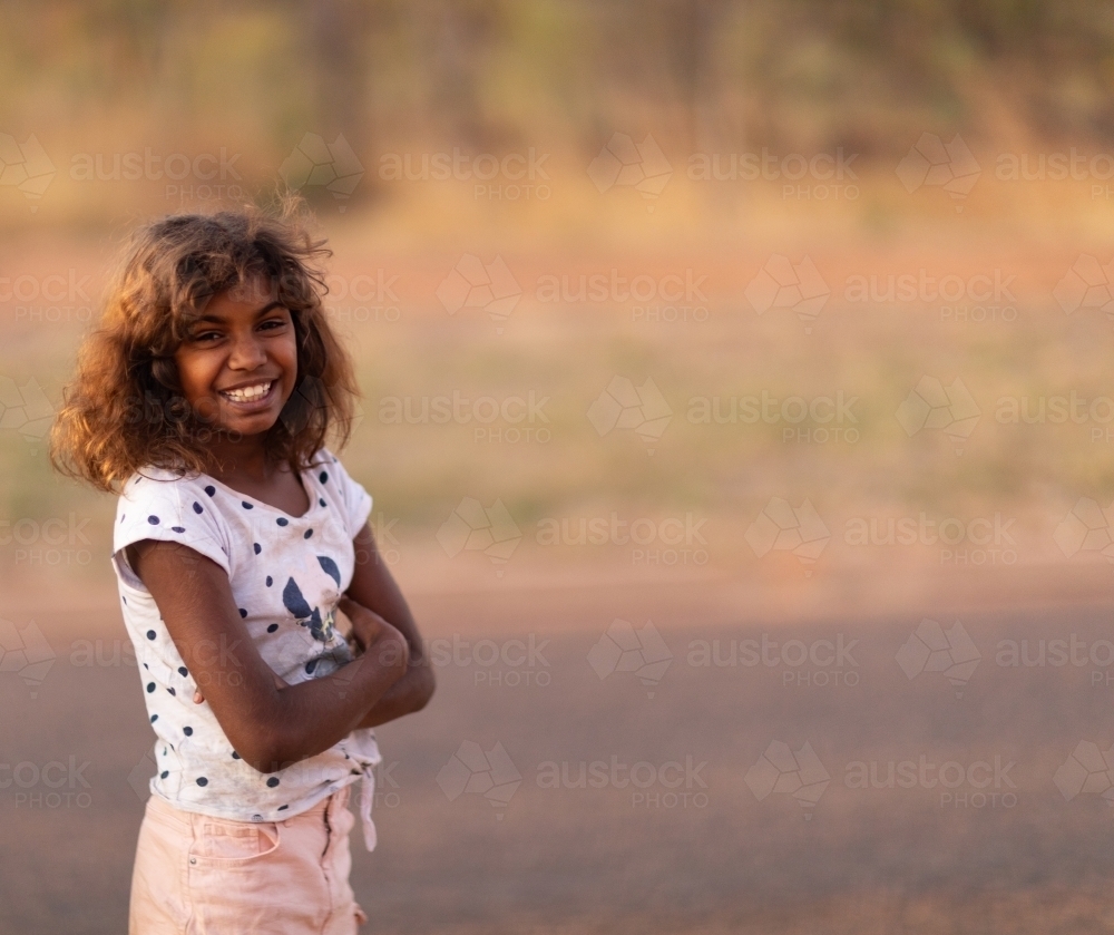 smiling young girl standing outdoors with arms crossed - Australian Stock Image
