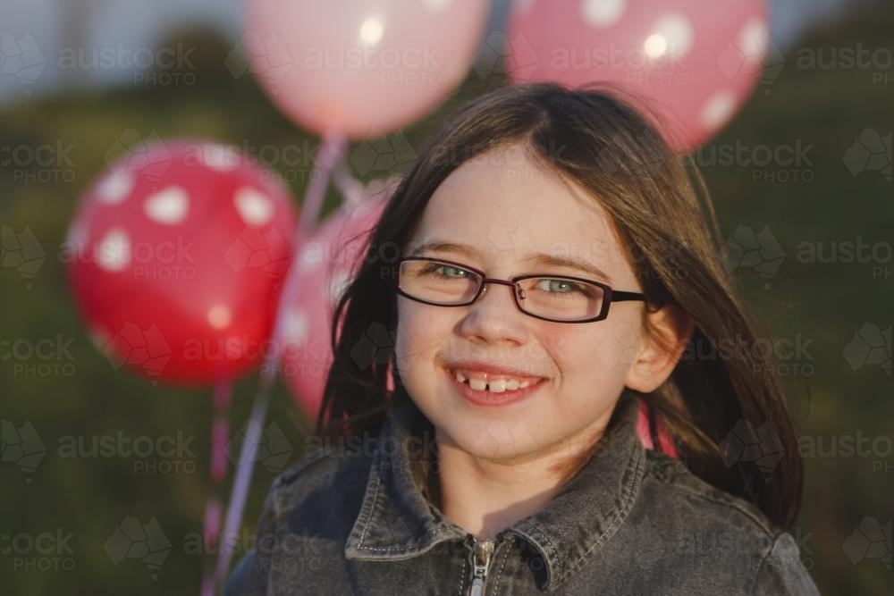 Smiling young girl with a bunch of pink balloons - Australian Stock Image