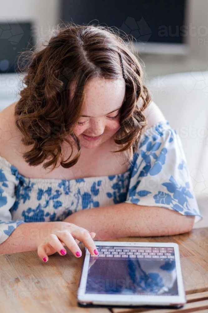 Smiling young person with Down syndrome using ipad technology typing - Australian Stock Image