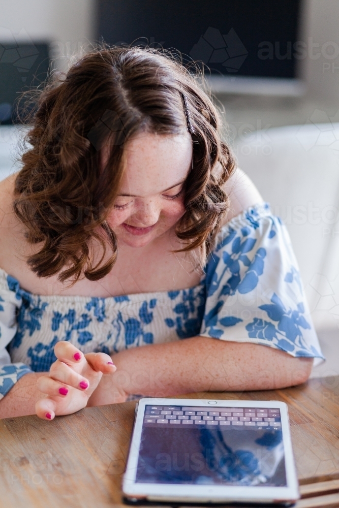 Smiling young person with Down syndrome using ipad technology typing - Australian Stock Image