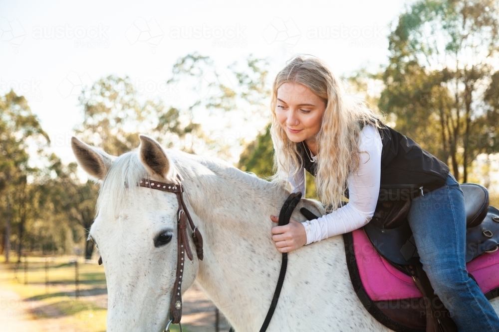 Smiling young teen lady sitting on her white horse in paddock - Australian Stock Image