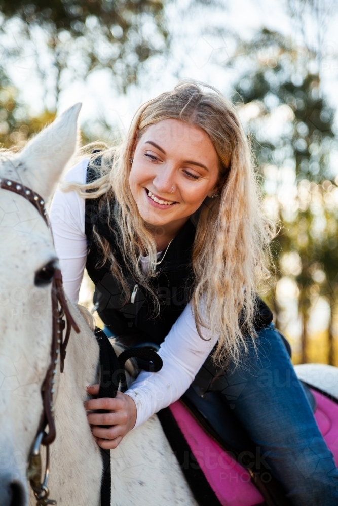 Smiling young teen lady sitting on her white horse in paddock - Australian Stock Image