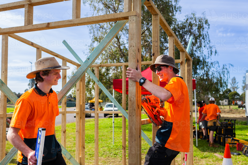 smiling young trade apprentices working together on building frame during hands on learning - Australian Stock Image