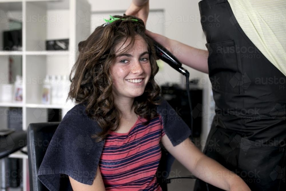 Smiling young woman having hair styled by hairdresser - Australian Stock Image